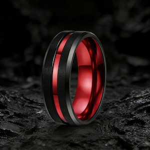 May include: A close-up of a black ring with a red interior. The ring has a textured black band with a thin silver band on either side. The interior of the ring is a vibrant red color.