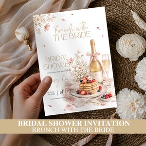 May include: A rectangular bridal shower invitation card featuring the text Brunch with the BRIDE and BRIDAL SHOWER. The design includes illustrations of a stack of pancakes with berries, a champagne bottle with a pink ribbon, and floral accents.