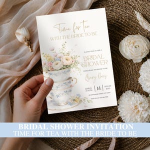 Può includere: Un invito bianco per addio al nubilato con un'illustrazione ad acquerello di tazze da tè impilate riempite di fiori color pastello. Il testo recita Time for Tea with the Bride to Be, Bridal Shower, Avery Davis, 14 agosto 2030 e i dettagli dell'evento.