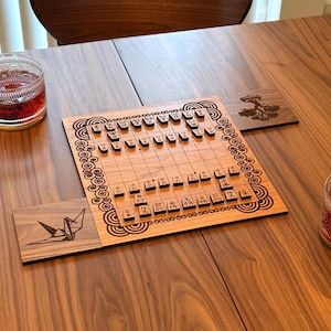 May include: A wooden Japanese Shogi board game with pieces arranged on a grid. The board is surrounded by decorative patterns. Two coasters with engraved designs of a crane and a tree are also present. Two glass cups of tea are on the table.