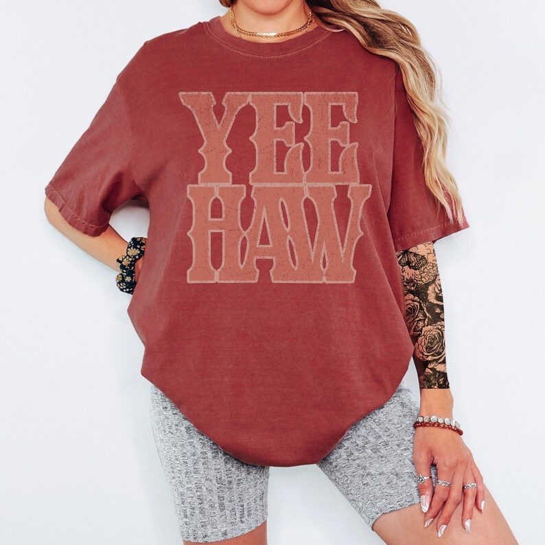 Pu&ograve; includere: Una maglietta color marrone con la scritta "YEE HAW" in un font in stile western. La maglietta &egrave; di colore pieno e ha una vestibilit&agrave; rilassata. Il testo &egrave; in una tonalit&agrave; pi&ugrave; chiara di marrone.
