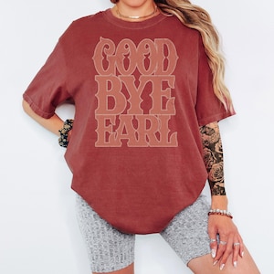 K&ouml;nnte beinhalten: Ein weinrotes T-Shirt mit dem Text "GOOD BYE EARL" in einer gestapelten Schriftart im Vintage-Stil. Das kurz&auml;rmelige Shirt hat eine lockere Passform. Der Text ist in einem helleren Weinrot gehalten.