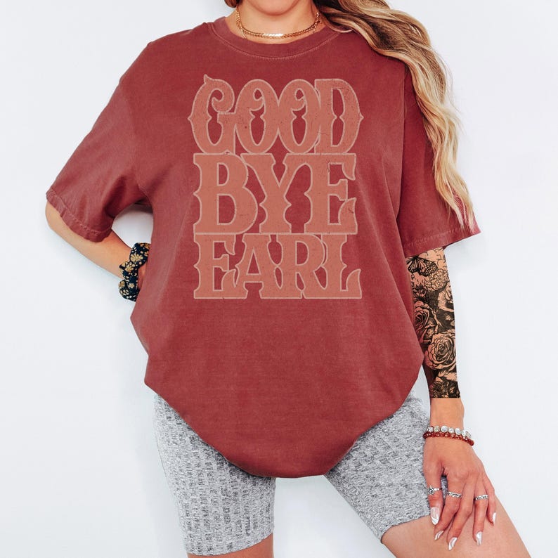 K&ouml;nnte beinhalten: Ein weinrotes T-Shirt mit dem Text "GOOD BYE EARL" in einer gestapelten Schriftart im Vintage-Stil. Das kurz&auml;rmelige Shirt hat eine lockere Passform. Der Text ist in einem helleren Weinrot gehalten.