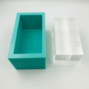 以下が含まれることがあります： ターコイズブルーのシリコンモールドと透明なアクリルブロック。モールドは長方形で、表面は滑らかです。アクリルブロックも長方形で、表面は滑らかです。