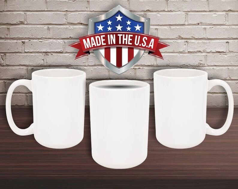 May include: Three white ceramic mugs and a white cylindrical cup are displayed on a dark brown surface against a brick wall. A shield-shaped emblem with the text "MADE IN THE U.S.A." is visible above the cups.