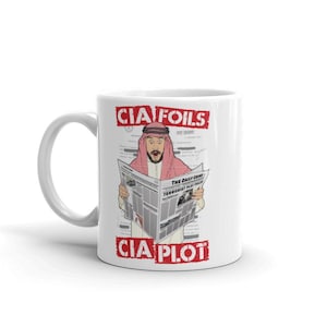 May include: White ceramic mug with a humorous graphic. The design features a cartoon illustration of a man in traditional Middle Eastern attire reading a newspaper with the headline "The Daily Grind: Terrorist Plot Foiled." The text "CIA FOILS CIA PLOT" is printed above and below the illustration.