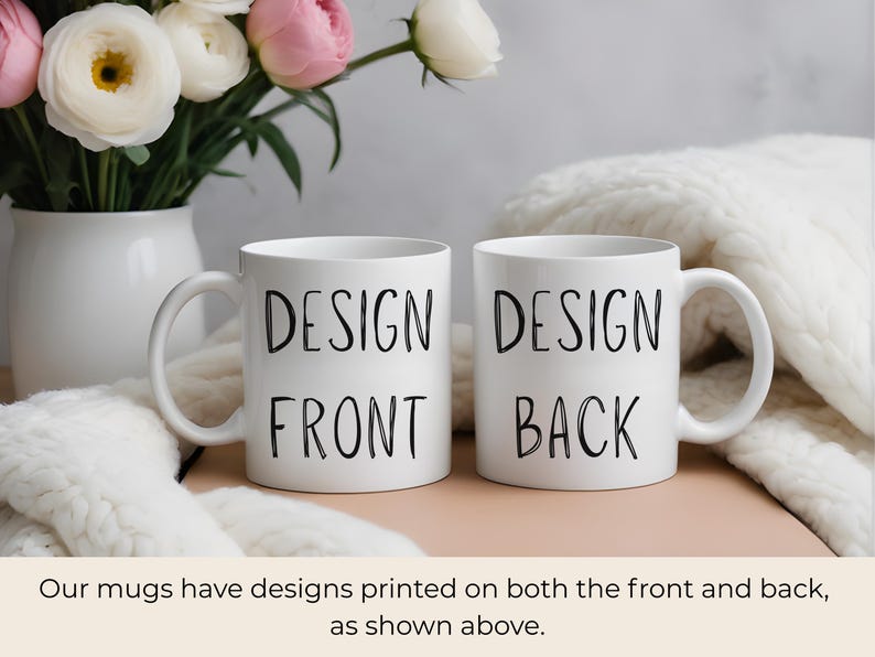May include: Two white ceramic mugs with black text that reads "DESIGN FRONT" and "DESIGN BACK". The mugs are on a light pink surface, with a white vase of flowers in the background. The flowers are white and pink.