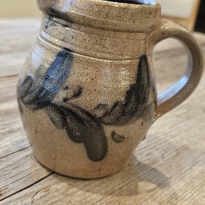May include: A stoneware pitcher with a speckled tan and beige finish, featuring a dark brown hand-painted brushstroke design around the body, a sturdy side handle, and a wide pouring spout at the top rim of the vessel.