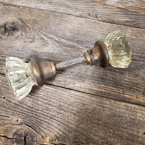 May include: A pair of antique glass door knobs with a brass finish. The knobs are clear glass with a fluted design. The knobs are attached to a metal rod.