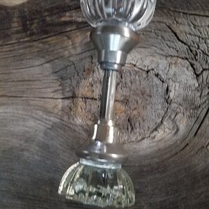 May include: A clear glass door knob with a silver metal base. The knob has a fluted design and is mounted on a wooden surface.