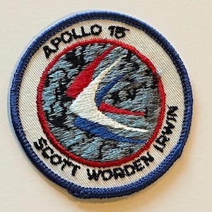 May include: Embroidered patch with a circular design. The patch features the text "APOLLO 15" and "SCOTT WORDEN IRWIN" in black lettering. The central design includes red, white, and blue elements, with a blue outer border.