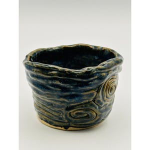 Könnte beinhalten: Ein handgefertigter Keramiktopf mit einem strukturierten, wirbelnden Design. Der Topf hat eine dunkelblaue Glasur mit goldenen und braunen Akzenten und einen rauen, organischen Rand. Der Innenraum ist tiefblau.