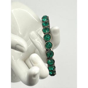 May include: A bracelet featuring a series of round, vibrant green faceted stones set in a dark metallic frame. The stones are arranged in a single vertical line, each held within a circular bezel setting, creating a continuous link design.