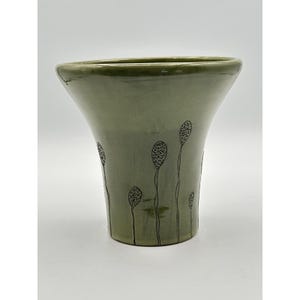 May include: A sage green ceramic vase with a flared rim and a smooth, glossy finish. The exterior features hand-drawn, thin black vertical lines topped with small, textured oval shapes that resemble seed pods or balloons scattered around the base.