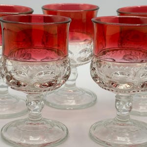 May include: A collection of five vintage wine glasses. Each glass has a clear, patterned base and a bright red upper bowl. The glasses have a classic, elegant design, suitable for serving wine or other drinks.