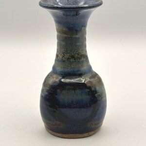 Könnte beinhalten: Eine handgefertigte Keramikvase mit ausgestellter Oberseite und rundem Körper. Die Vase weist eine Mischung aus blauen, braunen und grünen Farbtönen mit glänzendem Finish auf. Der Boden ist in natürlicher, unglasierter Tonfarbe gehalten. Ein dekoratives Stück für das Zuhause.