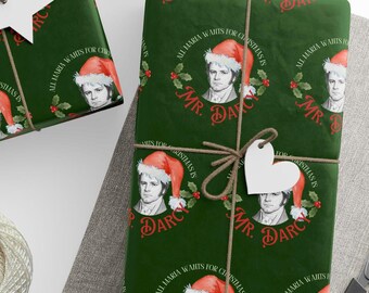 Peut inclure: Papier cadeau vert foncé avec un motif répété de Mr. Darcy portant un bonnet de Père Noël. Le texte dit "All Maria Wants for Christmas is Mr. Darcy". Le cadeau est ficelé avec de la ficelle.