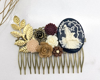 May include: An antique brass hair comb featuring a cameo of two figures under a tree. The comb is adorned with gold leaves and an assortment of flowers in shades of cream, brown, and burgundy.