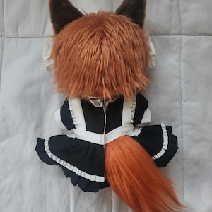 May include: A plush fox doll with a brown and orange color scheme. The doll is wearing a black and white maid outfit with a ruffled skirt. The fox has large, pointed ears and a fluffy tail.