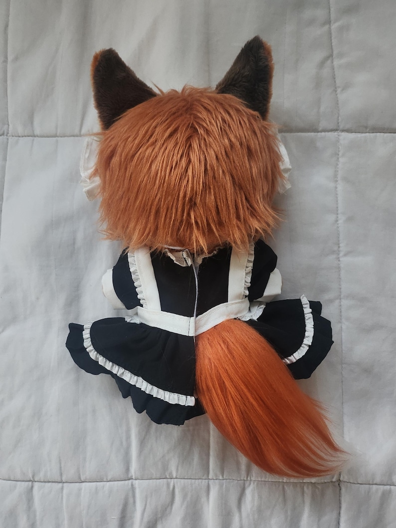 May include: A plush fox doll with a brown and orange color scheme. The doll is wearing a black and white maid outfit with a ruffled skirt. The fox has large, pointed ears and a fluffy tail.