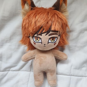 May include: A plush doll with orange hair and fox-like ears. The doll has a tan body, detailed facial features, and large, expressive eyes. The doll's hair is styled in a shaggy, layered cut. The ears are a mix of brown, orange, and tan.