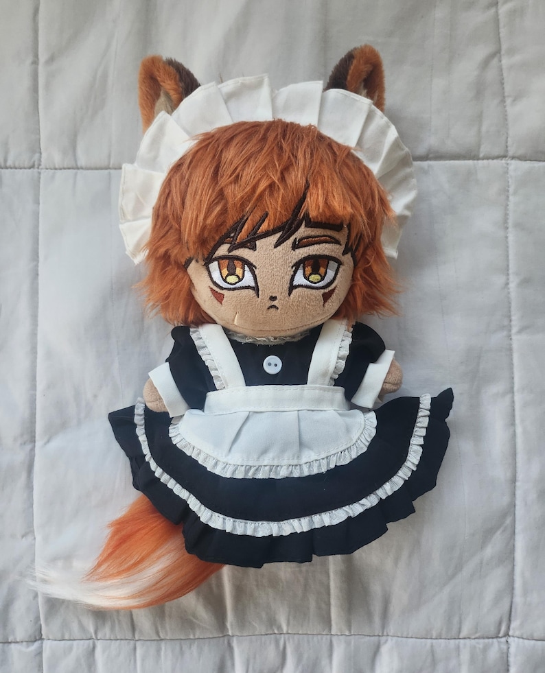 May include: A plush doll of a fox character wearing a black and white maid outfit, complete with a ruffled apron and a white cap. The doll has orange hair, fox ears, and a fluffy orange tail. The doll's eyes are large and detailed.