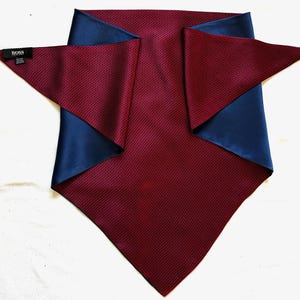 Puede incluir: Un pañuelo ascot de seda burdeos y azul marino. La tela burdeos tiene un sutil estampado geométrico. La tela azul marino es lisa y visible en el reverso. El pañuelo tiene una etiqueta BOSS.
