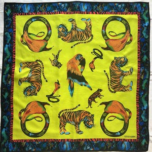Puede incluir: Un pañuelo cuadrado con un centro verde lima brillante que presenta ilustraciones de tigres, un loro y una cobra. El borde muestra un patrón de piel de serpiente azul y negro con una fina raya roja. El texto OTTO KERN está impreso abajo a la derecha.