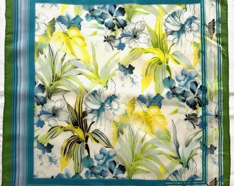 Könnte beinhalten: Quadratisches Seidentuch mit floralem Muster. Der Schal hat einen weißen Hintergrund mit blauen, gelben und grünen floralen Designs. Es hat einen türkisfarbenen Rand mit dünnen weißen Streifen und einen grünen Außenrand. Der Schal ist ca. 61 cm x 61 cm groß.
