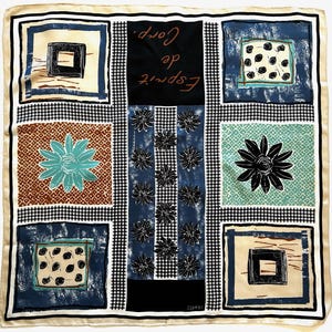 Op de afbeelding: Vierkante zijden sjaal met een crèmekleurige rand en een zwart-wit geruit patroon. De sjaal heeft verschillende vierkante ontwerpen met bloemen- en geometrische patronen in blauw, bruin en zwart. De tekst "Esprit de Corp" is gedrukt.