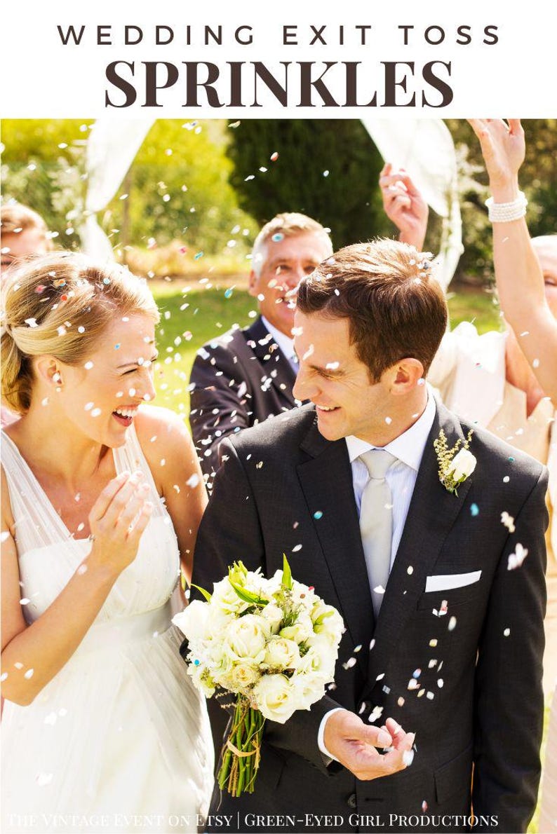 Puede incluir: Una novia y un novio caminan por el pasillo, sonriendo y riendo mientras cae confeti a su alrededor. La novia lleva un vestido de novia blanco y el novio lleva un traje negro con camisa blanca y corbata plateada. El novio lleva un ramo de flores blancas.