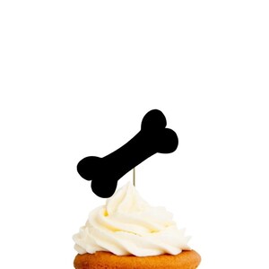 May include: Black cupcake topper shaped like a dog bone. The topper is on top of a frosted cupcake.