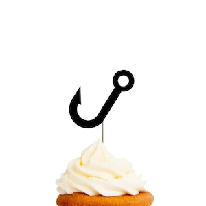 May include: A cupcake topped with a black fish hook cutout on a thin wooden pick. The text at the top reads CUPCAKE TOPPERS FISH HOOK. The bottom text reads THE VINTAGE EVENT ON ETSY | GREEN-EYED GIRL PRODUCTIONS. The cupcake has white frosting.