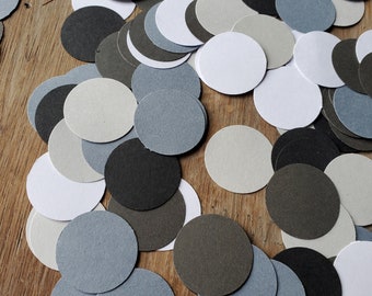 Puede incluir: Una colección de círculos de papel redondos en varios tonos de gris, blanco y negro. Los círculos están esparcidos sobre una superficie de madera.