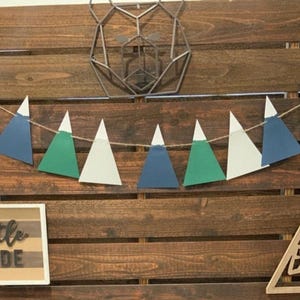 May include: A wooden backdrop with a geometric bear silhouette, a string of blue, green, and white triangle pennants, and a sign that says "Little Dude".