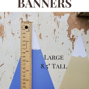 May include: Two paper mountain banner cutouts, one blue and one beige, with white peaks. The blue cutout is 8.5 inches tall and is measured with a ruler. The text "LARGE MOUNTAIN BANNERS" is at the top of the image and "LARGE 8.5" TALL" is at the bottom of the image.