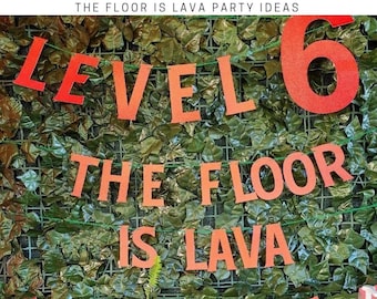 May include: A red and orange banner with the words "Level 6 The Floor Is Lava" hanging on a green wall with a green leafy background. There are also red and orange paper volcano cutouts hanging below the banner.