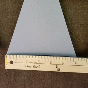 May include: A gray triangle-shaped paper banner with two holes punched at the top. The banner is hanging from a string. A wooden ruler with the words "One Yard" and "Made in China" printed on it is placed below the banner.