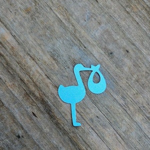 May include: Blue paper stork cutout holding a blue paper baby bundle. The stork is on a woodgrain background. Confetti Stork.