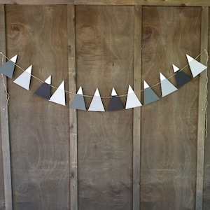May include: A paper banner with a string of gray, white, and black triangle shapes, resembling mountains. The banner is hanging on a wooden wall. The text "PAPER MOUNTAIN BANNERS SHOWN: GREYS" is at the top of the image.
