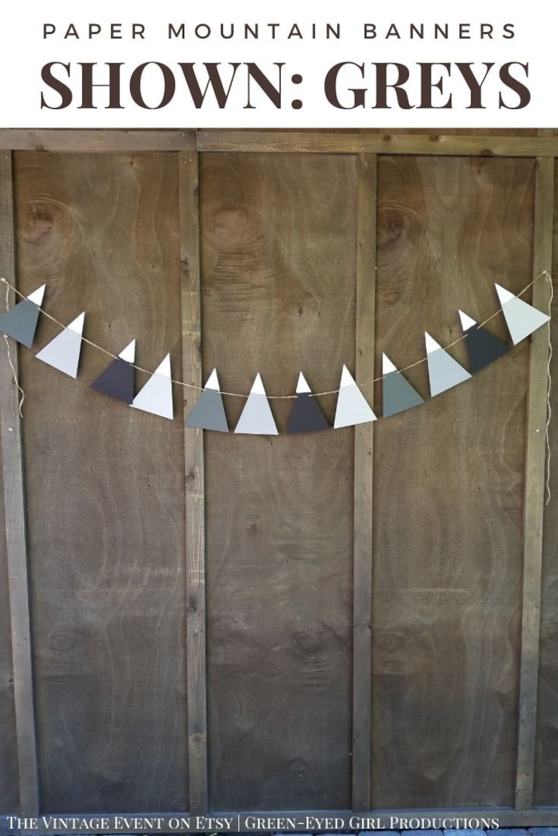 May include: A paper banner with a string of gray, white, and black triangle shapes, resembling mountains. The banner is hanging on a wooden wall. The text "PAPER MOUNTAIN BANNERS SHOWN: GREYS" is at the top of the image.