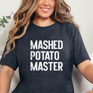 May include: Dark grey heather t-shirt with the text "MASHED POTATO MASTER" in white. The shirt is a short-sleeved crew neck style. The words "Dark Grey Heather" are printed at the bottom of the image.