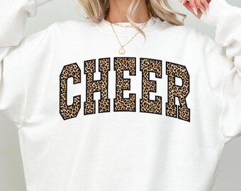 May include: White sweatshirt with the word "CHEER" in a leopard print design across the chest. The sweatshirt is a crew neck style. The word "White" is printed at the bottom left of the image.