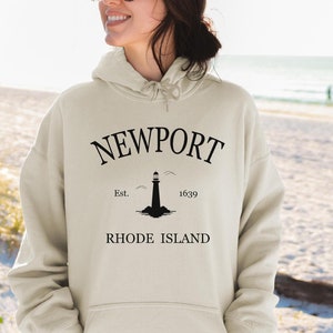 May include: A beige hoodie with a black graphic print of a lighthouse and the text "NEWPORT Est. 1639 RHODE ISLAND".