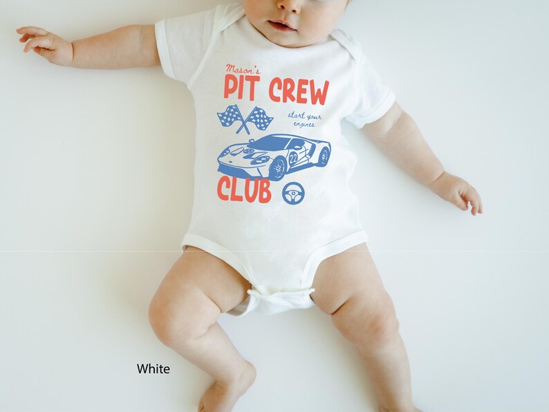 May include: White baby onesie with a red and blue graphic. The onesie features the text "Mason's PIT CREW CLUB" with a race car and checkered flags. The text "start your engines" is also included.