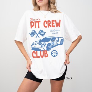 May include: White t-shirt with a red and blue graphic. The design includes the words "Mason's PIT CREW CLUB" with a blue race car, checkered flags, and a steering wheel. The phrase "start your engines" is also included.