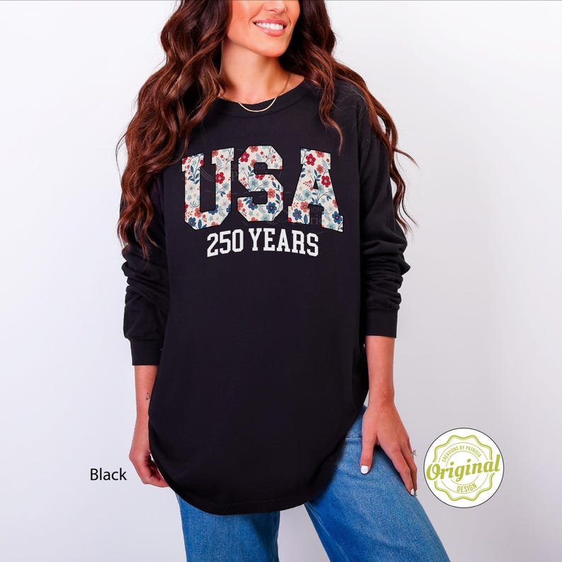 Puede incluir: Camiseta negra de manga larga con el texto blanco "USA 250 YEARS". Las letras "USA" est&aacute;n rellenas con un estampado floral de flores rojas, azules y blancas. Un estilo c&oacute;modo e informal.