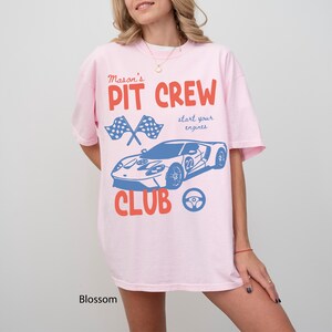 May include: A light pink t-shirt with the text "Mason's PIT CREW CLUB" in red and blue. The shirt features a blue race car graphic, crossed checkered flags, and the phrase "start your engines."
