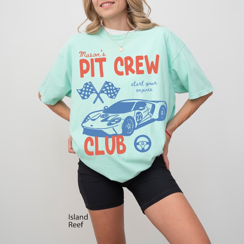 May include: A light green t-shirt with the words "Mason's PIT CREW CLUB" in red and blue. The shirt features a blue race car graphic, crossed checkered flags, and a steering wheel. The text "start your engines" is also included.