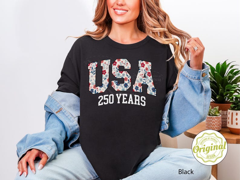 Puede incluir: Sudadera negra de cuello redondo con la palabra "USA" en estampado floral y el texto "250 YEARS" en blanco. La sudadera forma parte de una colecci&oacute;n de ropa.